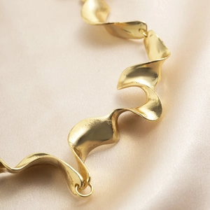 Primer plano de collar dorado ondulado con textura sobre tela de seda champán