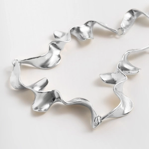 Detalle del collar metálico plateado con cinta retorcida y eslabones geométricos fluidos