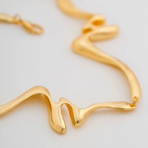 Detalle del collar dorado con curvas orgánicas y un acabado metálico líquido
