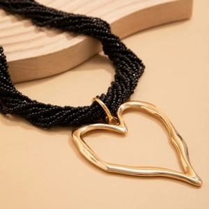 Détail d'un collier à perles noires multicouches avec pendentif coeur doré texturé