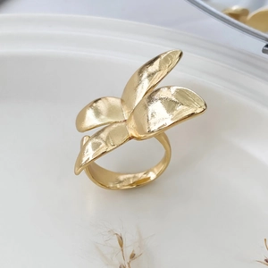 Macro detail of gold-plated petal ring with hammered texture on a ceramic tray