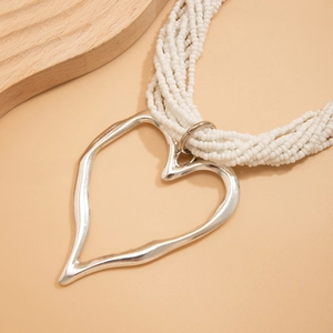 Détail d'un collier de perles blanches multicouches avec grand pendentif cœur argent mat