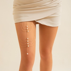 Detail of multi-layer golden thigh chain with elegant white pearls on model's leg