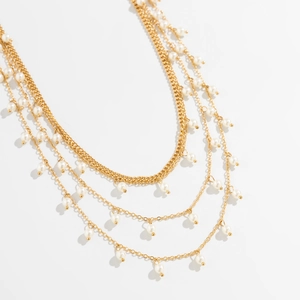 Detail of layered gold metal chain with elegant round white faux pearl pendants