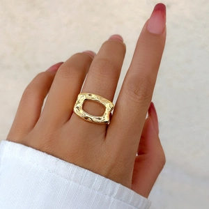 Detailed close-up of a hollow rectangular gold ring with hammered texture worn on a finger