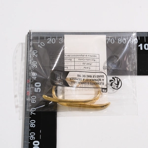Detailed view of large gold metallic ribbon ring next to a measuring ruler for size