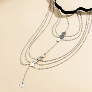 Macro detail of layered silver leg chain featuring polished sequins and black velvet strap