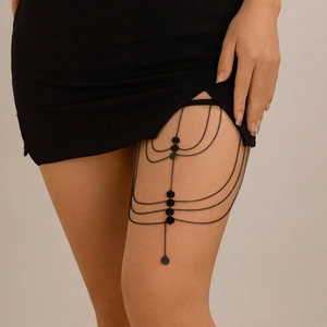 Detail of layered black leg chain with metallic sequins on female thigh