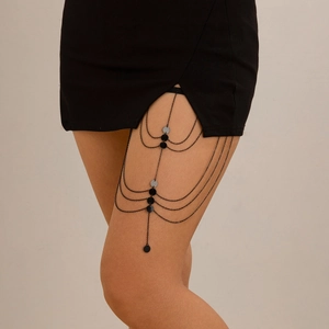 Detail of multi-layered black metal leg chain with round sequin pendants on thigh