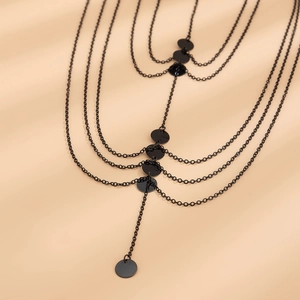 Macro detail of multi-layered black metal leg chain with smooth round charms and tassels