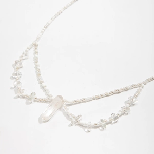 Detalle de un collar de varias capas con cuentas blancas y colgante de cristal claro