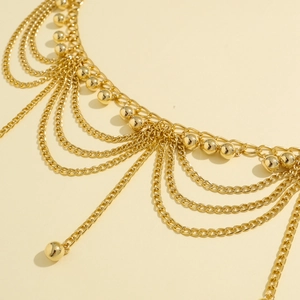 Detail of layered gold waist chain featuring polished metal beads and fringe design