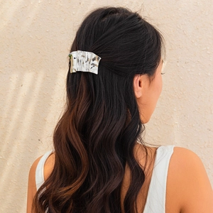 Detailed view of silver metallic pleated hairpin with irregular texture on wavy hair