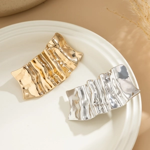 Detail of irregular textured gold and silver metal hairpins on a beige ceramic plate