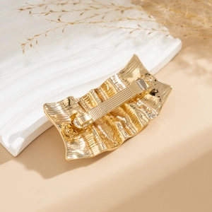 Detailed view of golden wavy metal hairpin with brushed texture and spring clip back