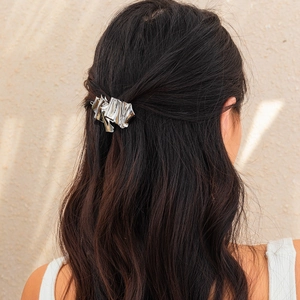 Close-up of a silver crumpled metal hairpin on brown wavy hair with soft shadow