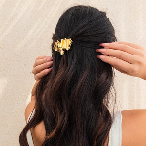 Detail showing irregular gold metal wrinkled hairpin on dark wavy hair for elegant styling