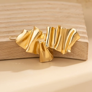 Detailed view of golden hairpin with irregular crumpled metal texture on a wooden block