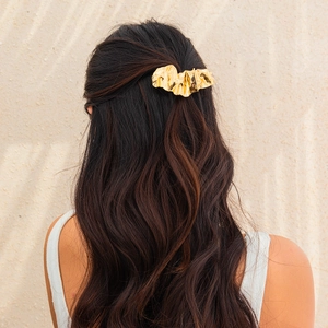 Detail view of irregular gold crinkled metal hairpin worn on wavy brunette hair