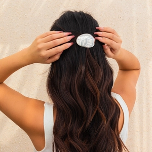 Close-up of a silver oval hairpin with shell texture on wavy brown hair for elegant styling