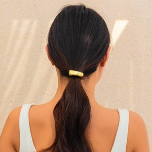 Close-up of a minimalist gold metal cuff hairpin on a model's low ponytail style