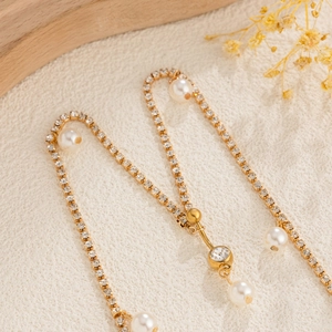 Detalle de la cadena corporal dorada con brillantes de imitación y perlas blancas
