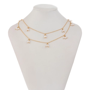 Détail d'un collier double rang doré avec pendentifs perles sur un buste blanc