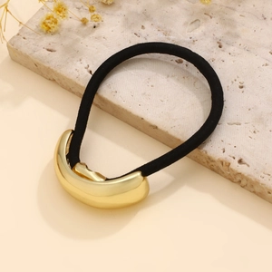 Close-up of a glossy gold metal hairpin with elastic hair tie on a stone tray