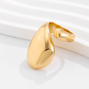 Gros plan d'une grande bague goutte dorée au design fluide sur un support blanc ondulé