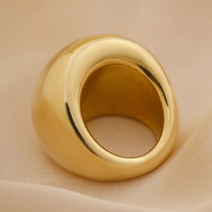 Détail macro d'une bague dôme dorée polie sur un tissu en soie champagne luxe