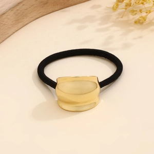 Close-up of golden irregular metal hair tie on wood tray with decorative dried flowers