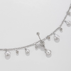 Detalle de cadena corporal plateada con perlas, colgantes de strass y una barra curvada