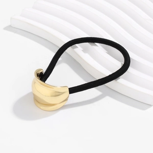 Detailed macro view of the polished golden curved metal ornament on a black elastic hair tie