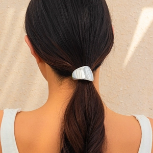 Detailed view of an irregular folded metal hairpin in silver on a ponytail