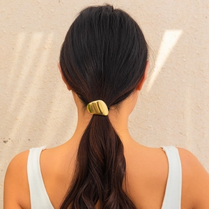 Detail of golden wrinkled metal hairpin hair cuff on model's ponytail with tree shadows
