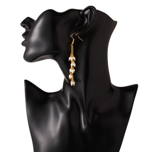 Boucles d'oreilles pendantes dorées avec perles blanches sur un mannequin noir élégant