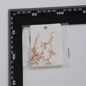 Vue détaillée des boucles d'oreilles pompon dorées avec perles et règle de 6 cm
