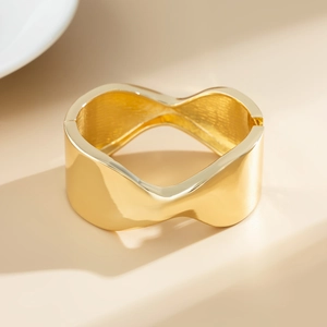 Dettaglio di un ampio bracciale dorato ondulato con finitura a specchio e design moderno