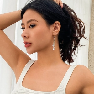 Détail d'une boucle d'oreille longue en perle avec étoile argentée sur un modèle féminin