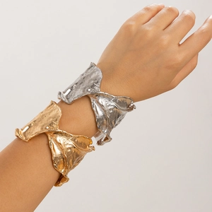 Primer plano del brazalete ancho con textura irregular en acabado dorado y plateado