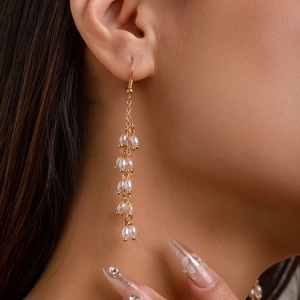 Élégantes boucles d'oreilles pendantes dorées avec perles blanches sur un mannequin