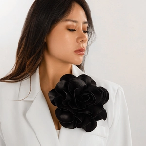 Close-up of a large black satin rose brooch pinned on a white blazer lapel