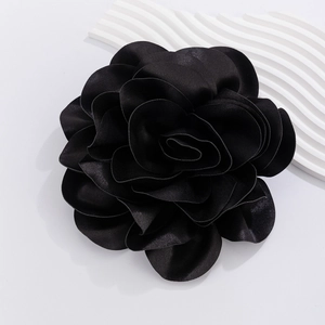 Detail view of large black satin rose brooch with layered fabric petals on white surface