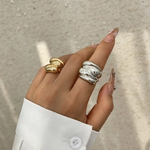 Close-up of chunky gold and silver irregular textured rings styled with white cuff