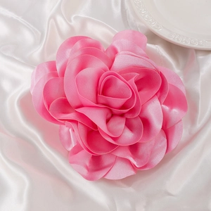 Detailed top view of soft pink satin rose brooch with layered petals on fabric