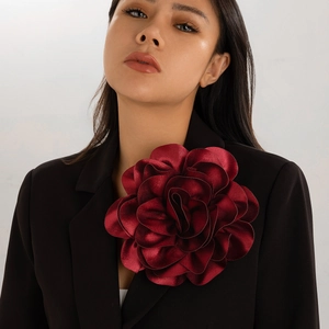 Macro detail of large deep burgundy satin rose brooch pinned to a black blazer lapel