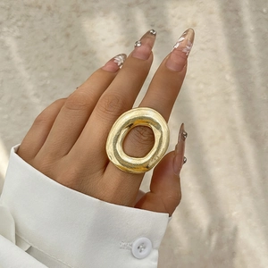 Detailed close-up of a large chunky oval ring in golden brushed metal on finger