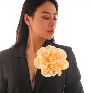Detailed view of oversized apricot satin rose brooch pinned to a black suit lapel
