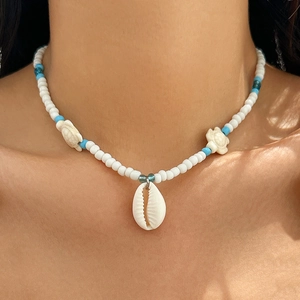 Detail of beach-style beaded necklace with white shell pendant and small turtle beads