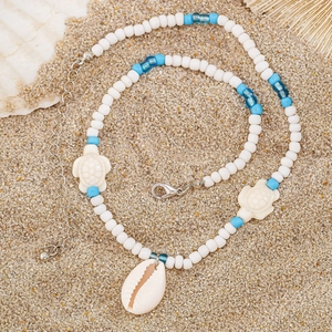 Detail of beach necklace with white beads, blue accents, sea turtle and conch charms